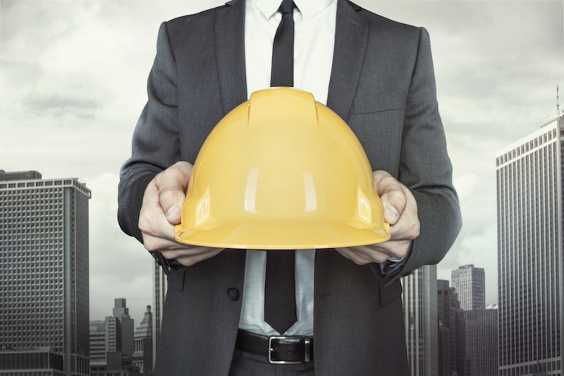 Businessman holding yellow helmet in hands with tie and shirt on cityscape background