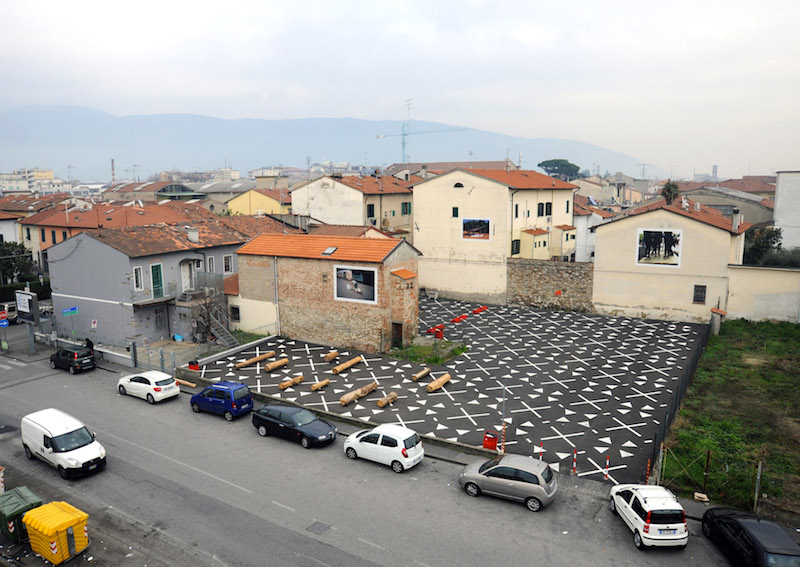 Il progetto converte un vuoto urbano, precedentemente destinato a parcheggi, in piazza pubblica aperta ai cittadini. L’intervento ha un profondo impatto sulla vivibilità del quartiere, creando un’area di integrazione aperta alle iniziative comuni, nella zona densamente edificata del Macrolotto Zero, in cui l’assenza di spazi pubblici è un problema evidente. Il nuovo perimetro è definito orizzontalmente dalla pavimentazione ispirata a un mosaico che impreziosisce lo spazio e verticalmente dalle installazioni fotografiche che raccontano il valore simbolico del progetto, poste sulle facciate dei tre palazzi tangenti alla piazza.